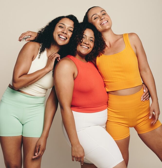 Three_women_wearing_fitness_gear_in_different_colors_smiling_and_posing_together.