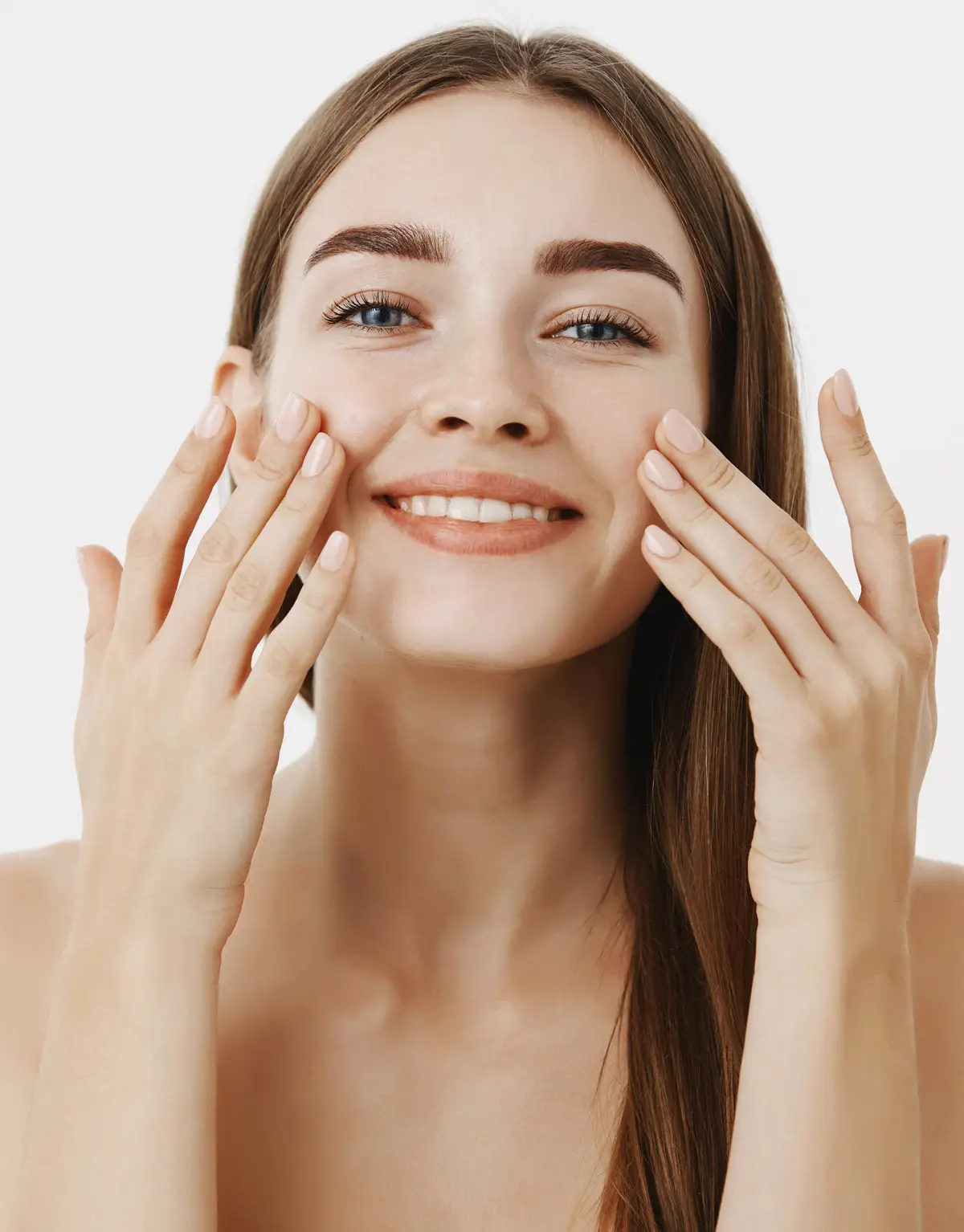 Young woman smiling and gently touching her cheeks with both hands, looking happy and confident.